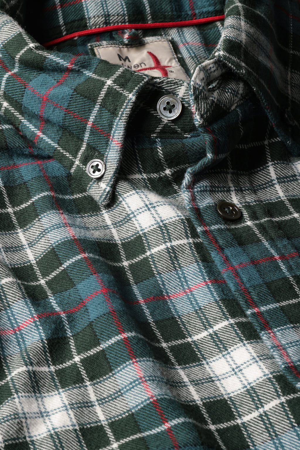 Close-up of a plaid button-down shirt in dark green, white, and light blue with thin red accent lines, showing the collar, buttons, and inner neck label.
