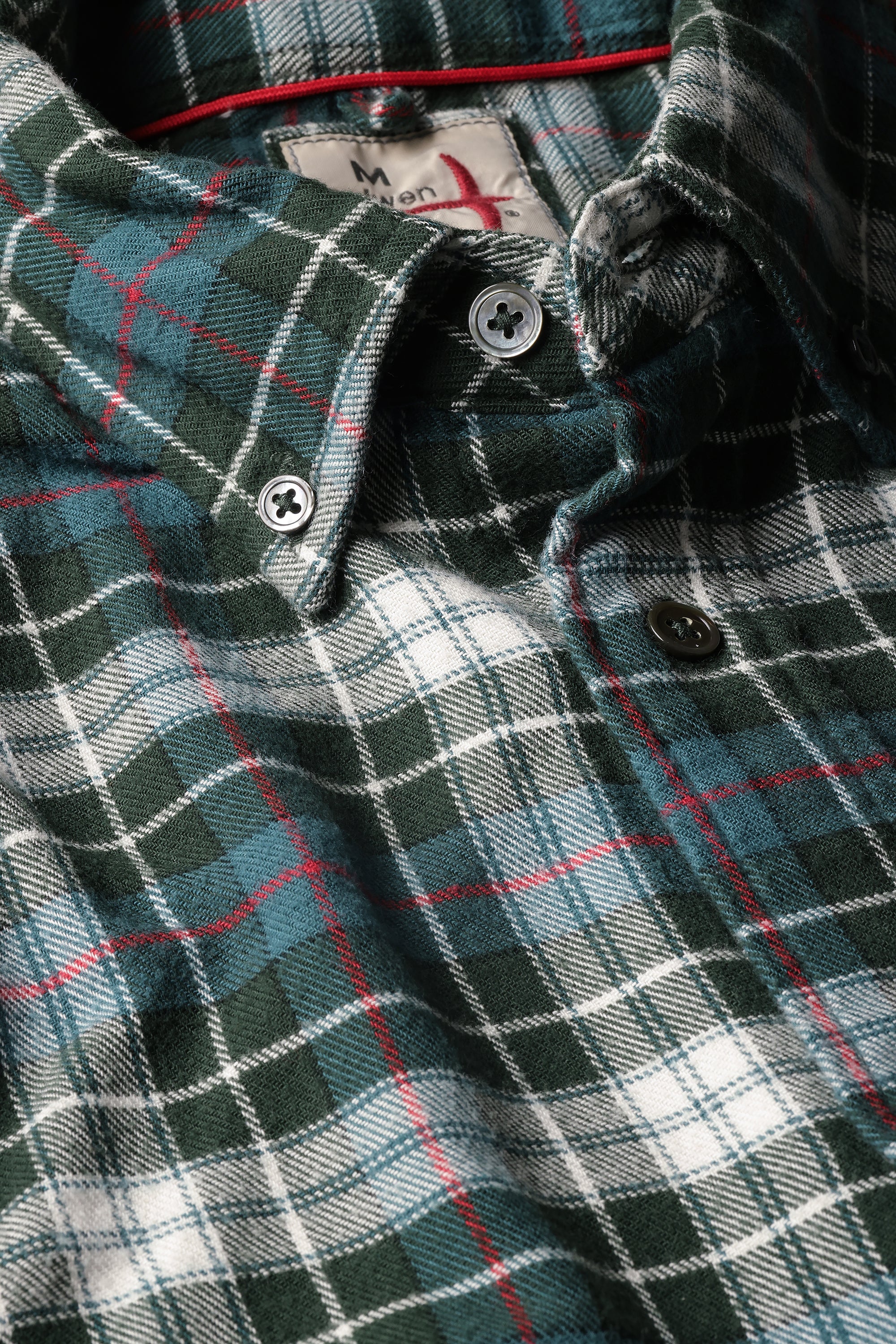 Close-up of a plaid button-down shirt in dark green, white, and light blue with thin red accent lines, showing the collar, buttons, and inner neck label.