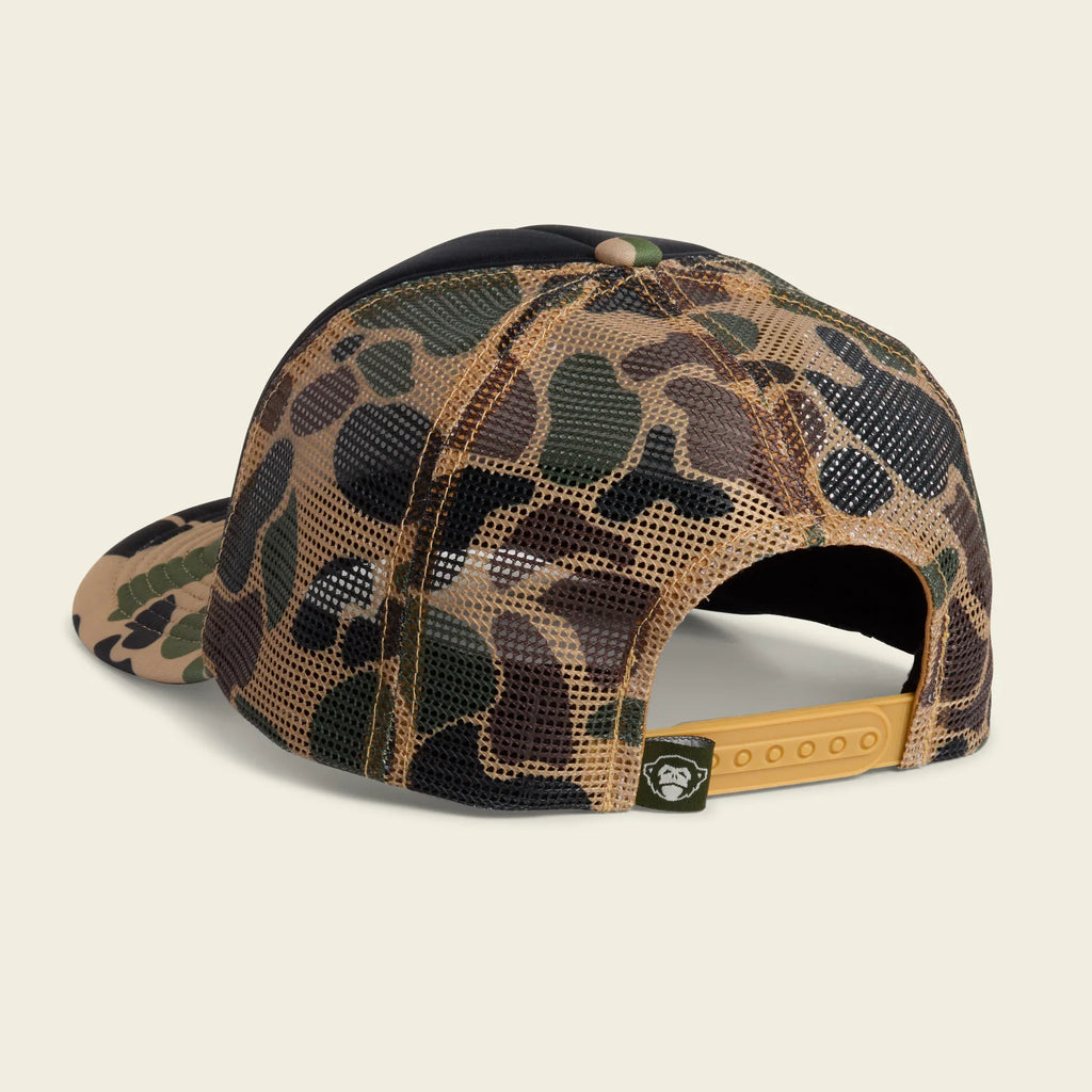 A camouflage trucker cap with a brown mesh back and a tan adjustable strap, shown from a three-quarters angle on a light beige background.