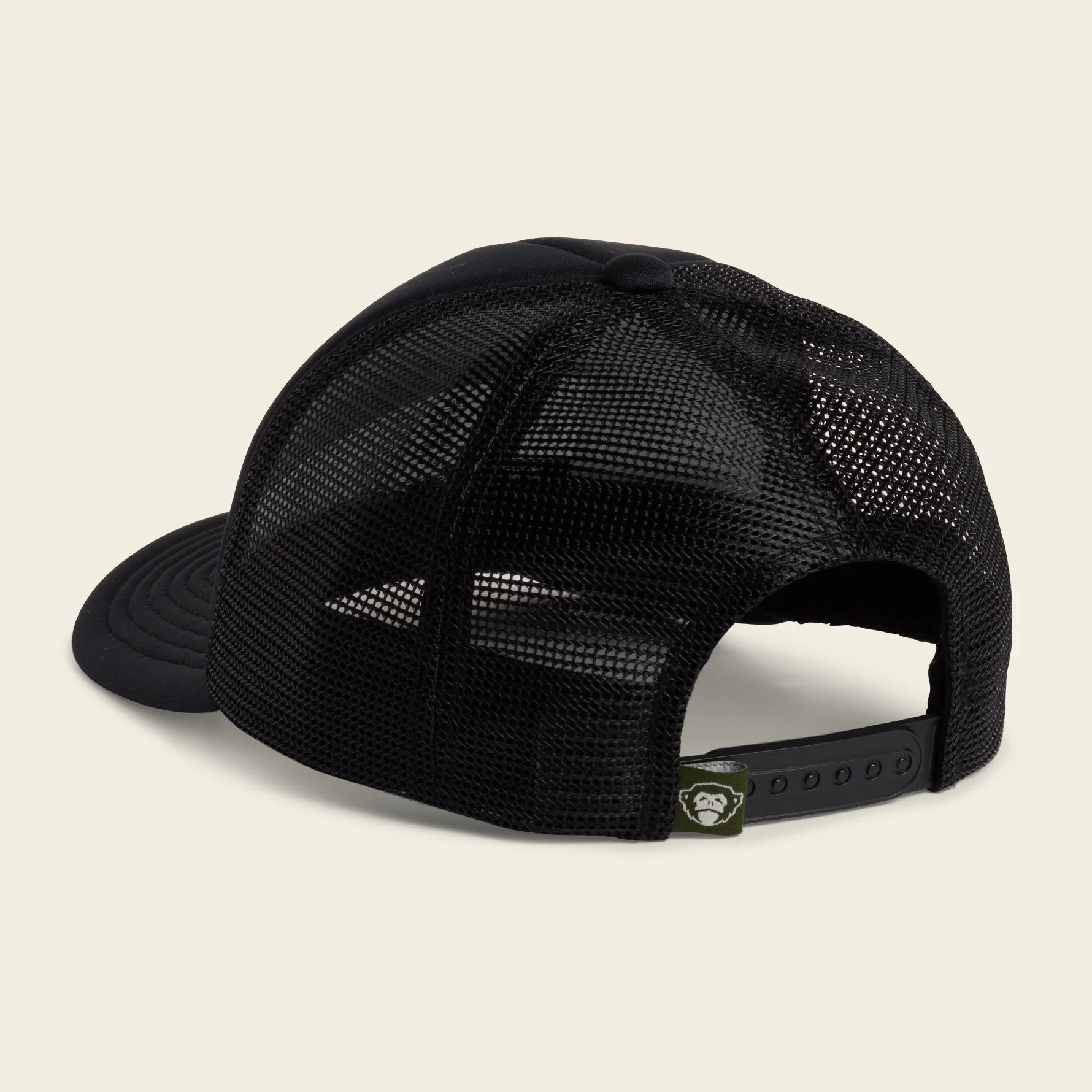 A black trucker-style cap with a black mesh back and solid black visor, shown from a three-quarters angle on a light cream background.
