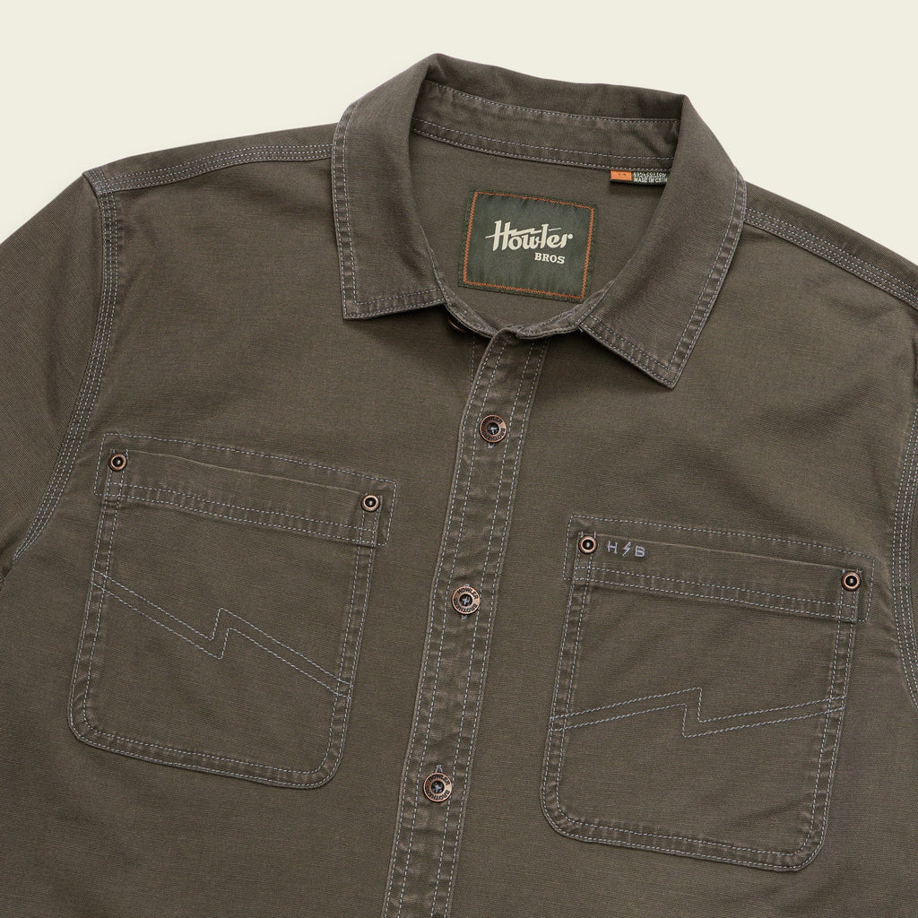 A close-up of a dark olive brown button-down shirt by Hosier 8013, featuring two chest pockets with zigzag contrast stitching and a visible brand label on the inner collar.
