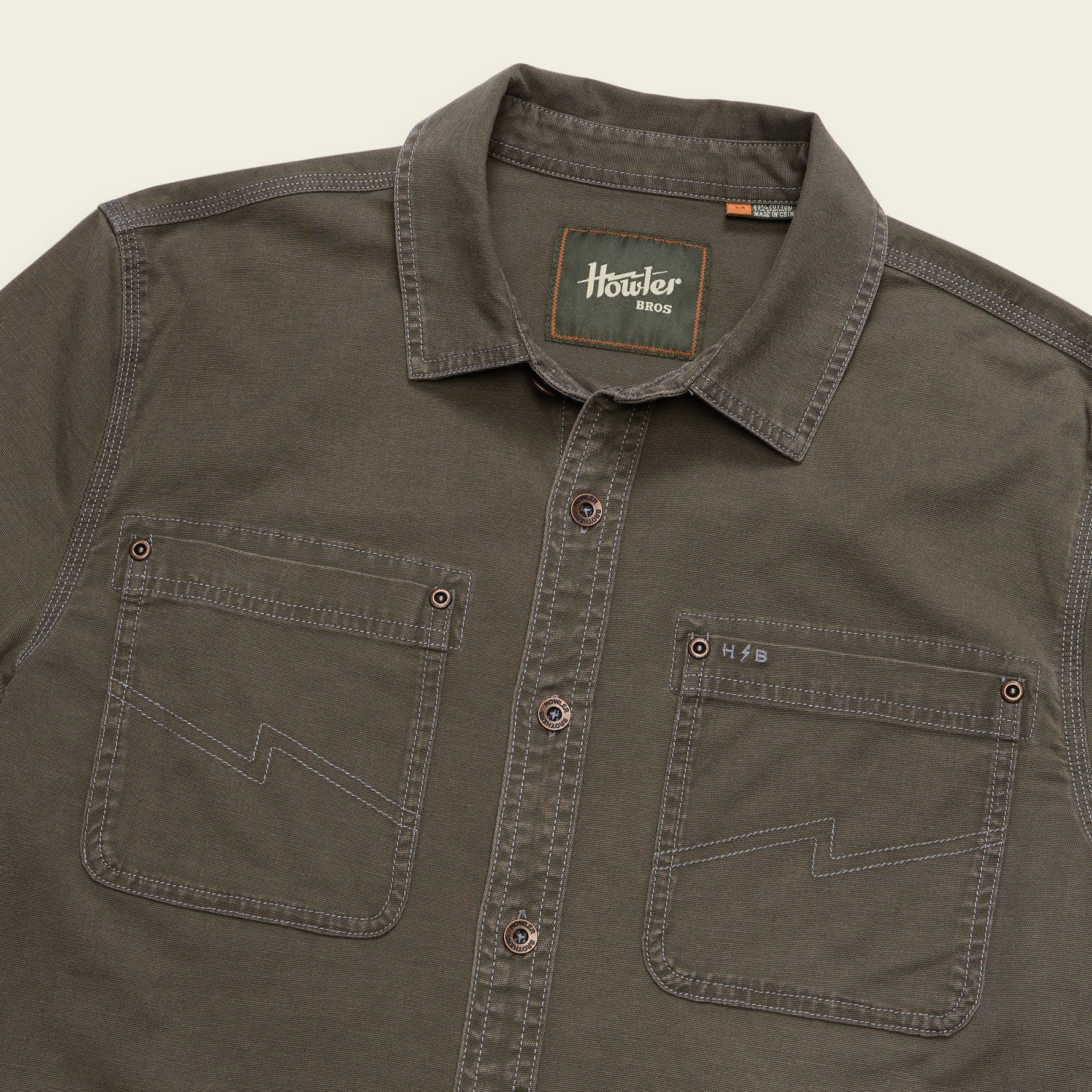 A close-up of a dark olive brown button-down shirt by Hosier 8013, featuring two chest pockets with zigzag contrast stitching and a visible brand label on the inner collar.