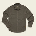 A dark olive brown long-sleeve button-up shirt with two chest pockets, laid flat on a light cream background. The brand 'Brixton' is visible on the inner neck label and a small patch near the lower right hem.