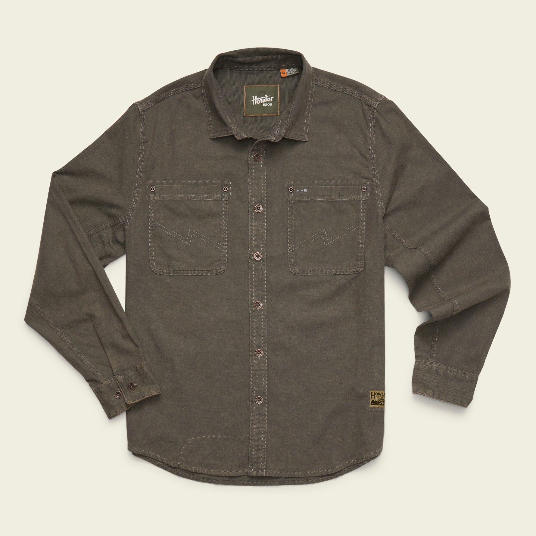 A dark olive brown long-sleeve button-up shirt with two chest pockets, laid flat on a light cream background. The brand 'Brixton' is visible on the inner neck label and a small patch near the lower right hem.