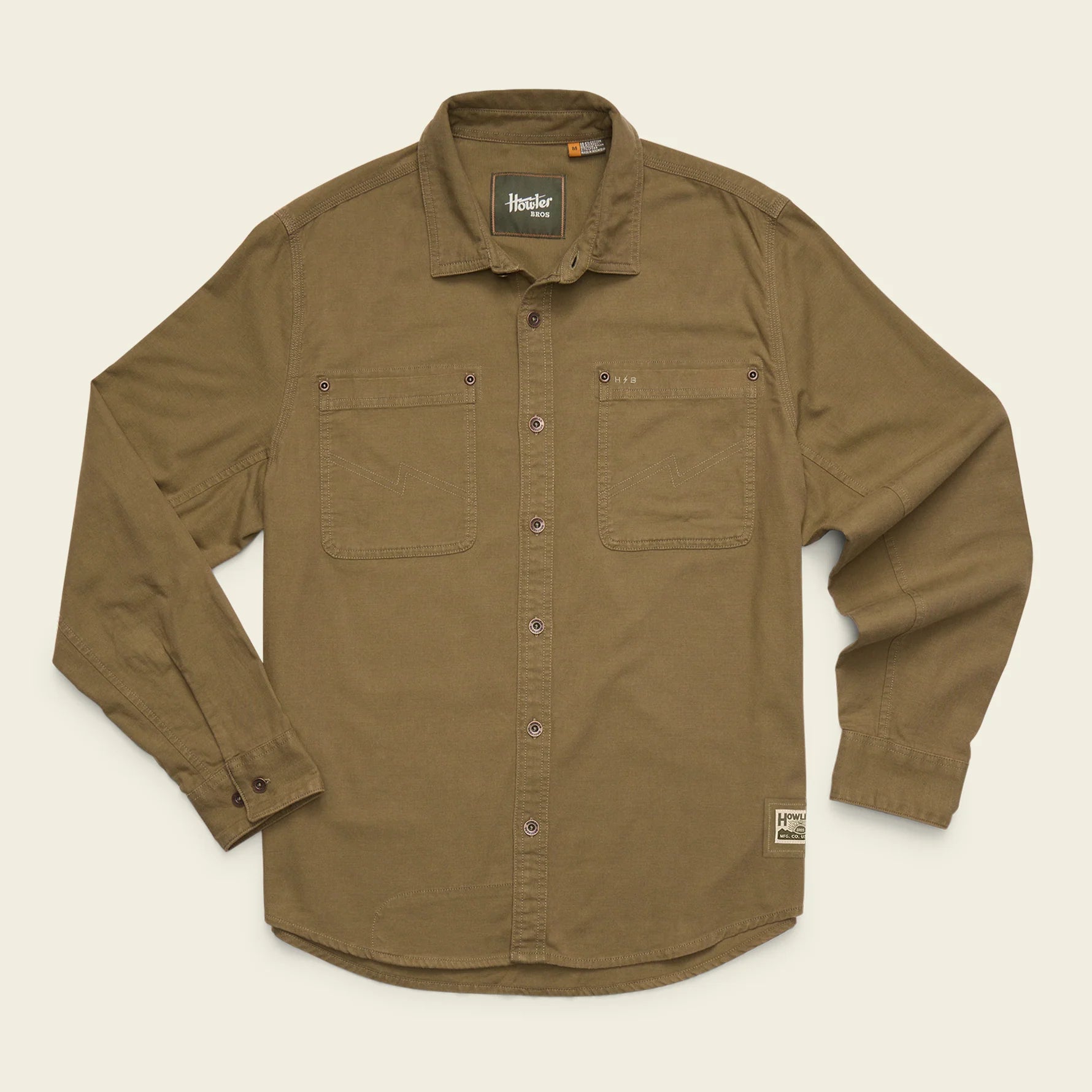A brown long-sleeve button-up shirt with two chest pockets, laid flat on a light beige background. The brand 'Helly Hansen' is visible on the inner neck label and a small hem tag.
