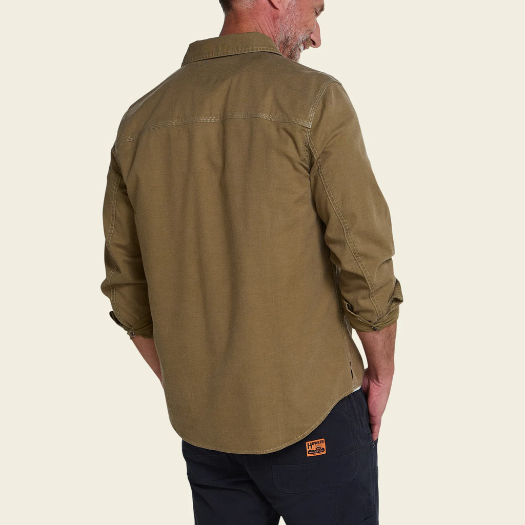 A man shown from the back wearing a muted olive-brown long-sleeve button-up shirt and dark navy pants, against a plain light beige background.