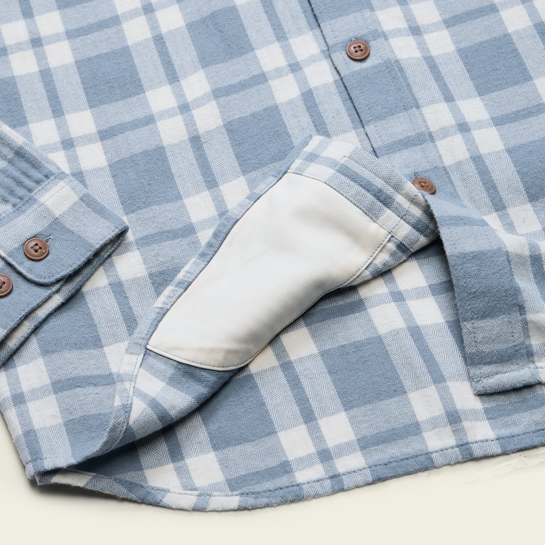 Close-up of a light blue and white plaid button-up shirt with brown buttons and a white elbow patch.