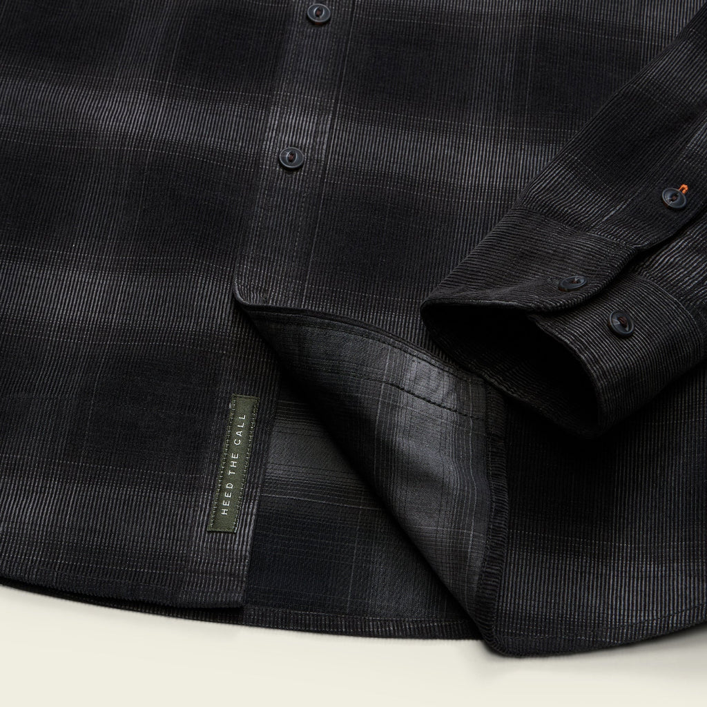 Close-up of a dark charcoal plaid button-down shirt with a folded cuff showing the button placket and a small fabric brand tag reading 'RED FINE CLOTH'.