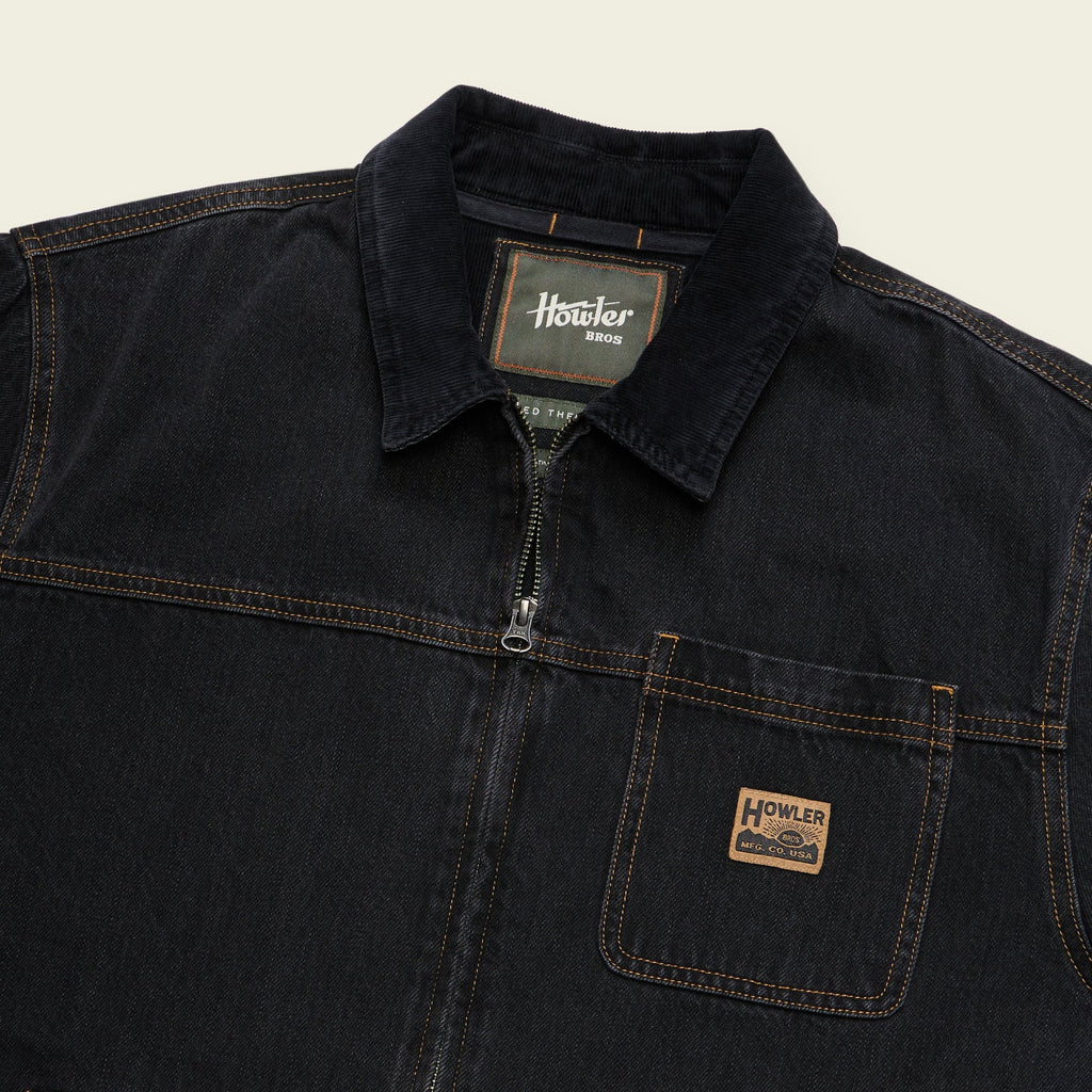 Close-up of a dark indigo denim work shirt by Howler, featuring a collar, half-zip front, and a chest pocket with a brand patch.