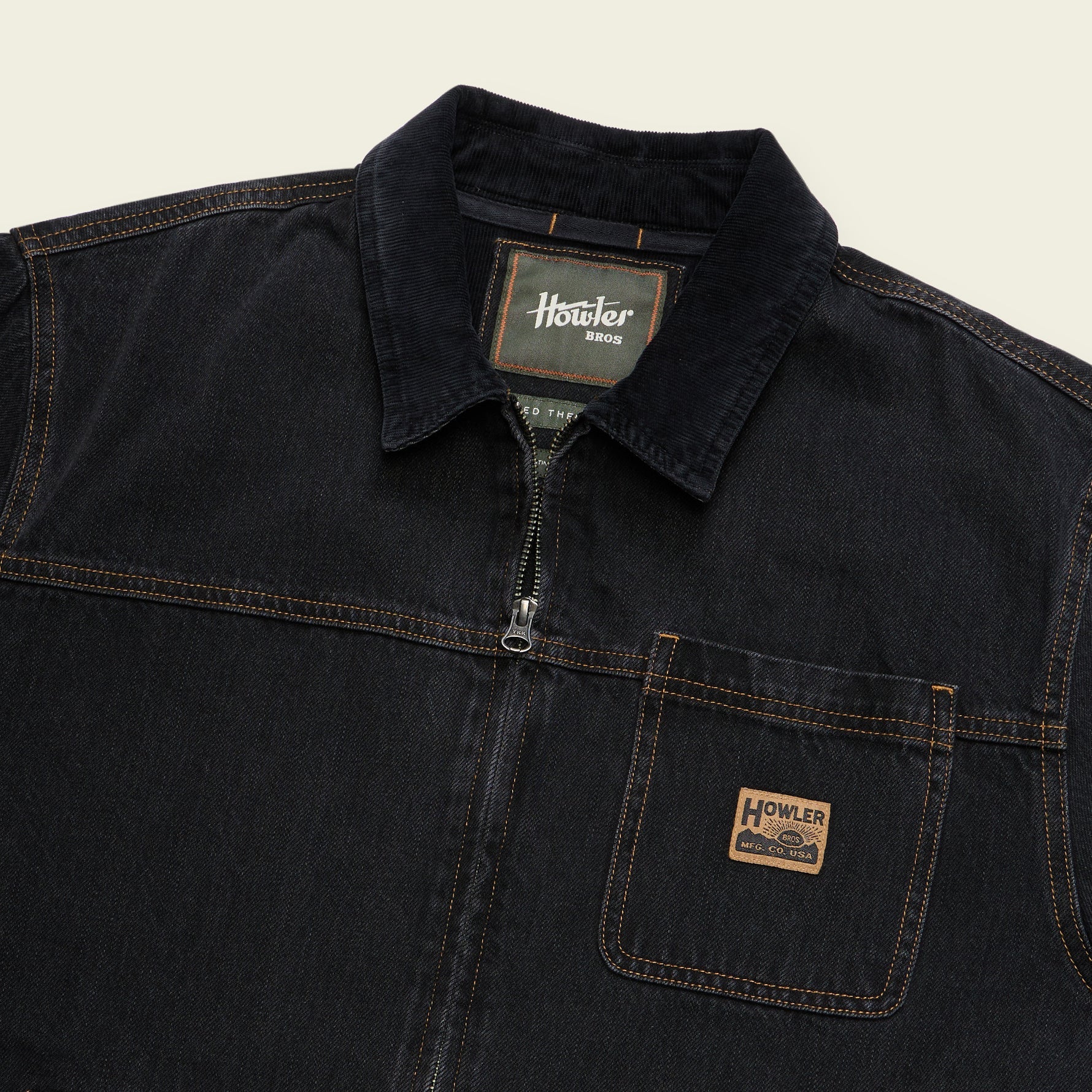 Close-up of a dark indigo denim work shirt by Howler, featuring a collar, half-zip front, and a chest pocket with a brand patch.