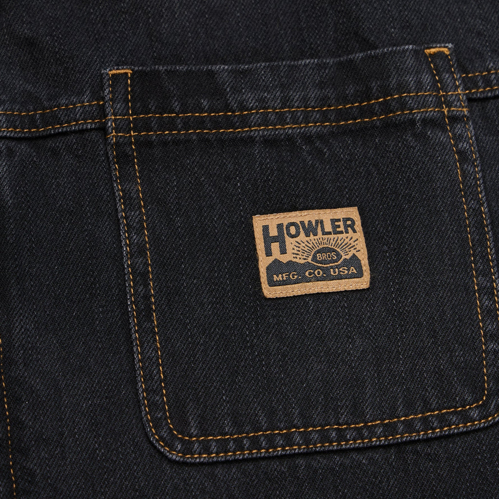 Close-up of a dark indigo denim back pocket with contrast tan stitching and a rectangular Howler Brand patch sewn onto the pocket.