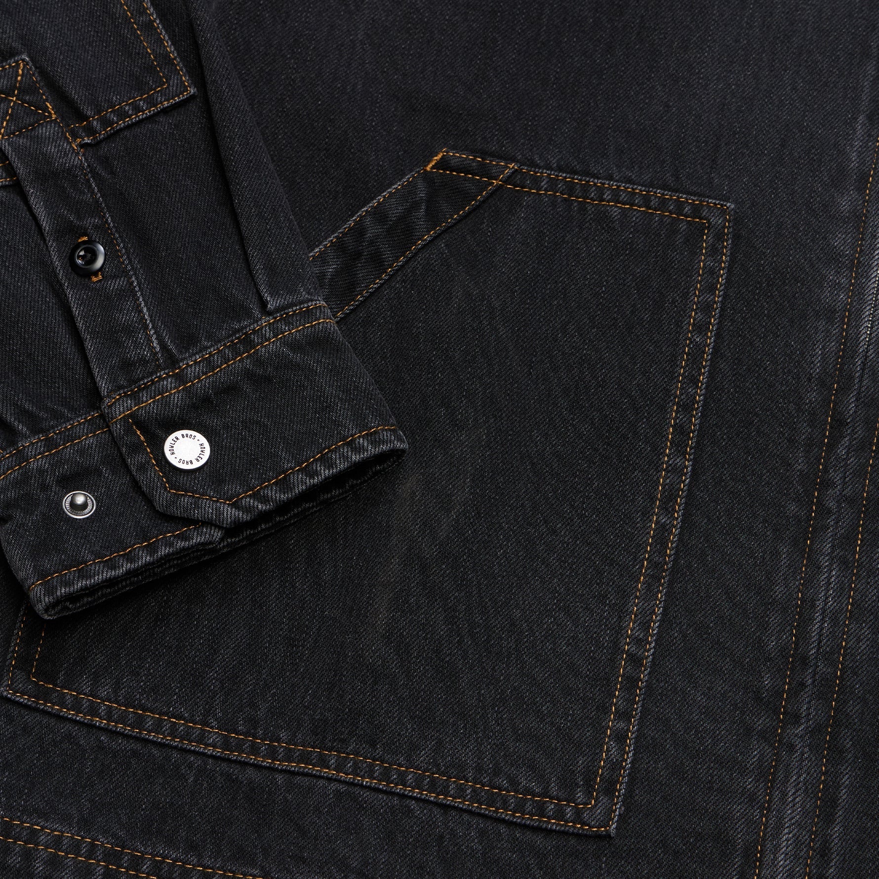 Close-up of a dark washed denim garment showing a pocket, buttoned cuff, and contrast stitching.