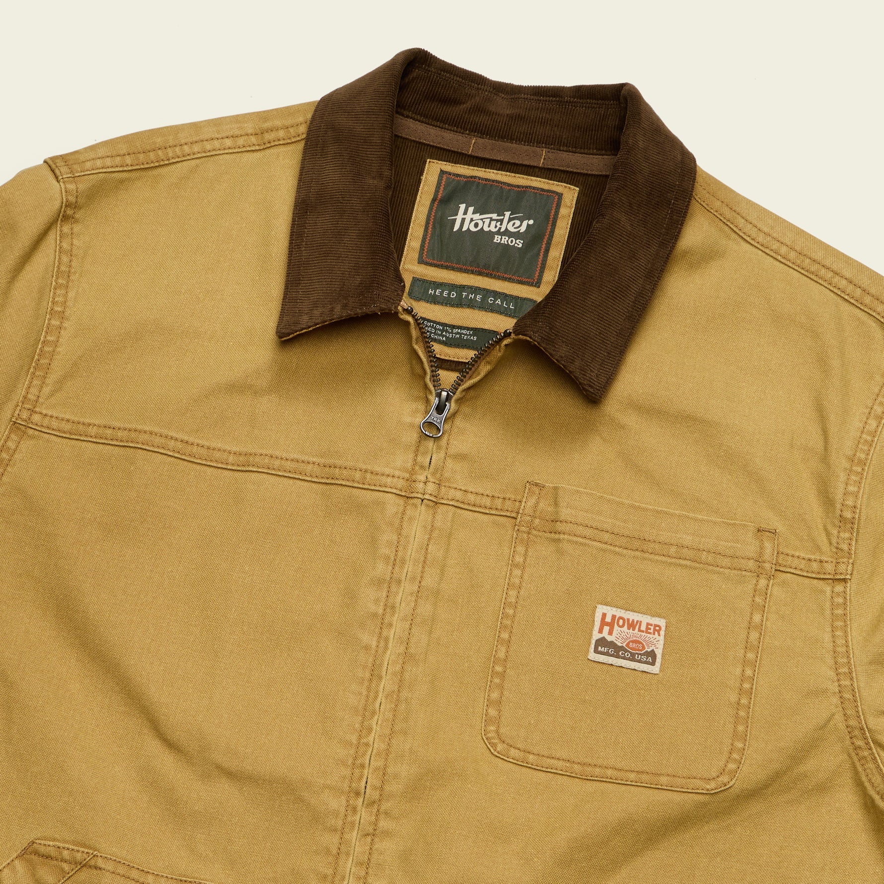 A close-up of a Howler Wags work jacket in a warm tan color with a contrasting dark brown corduroy collar and a front zipper. The brand logo is visible on the chest pocket.