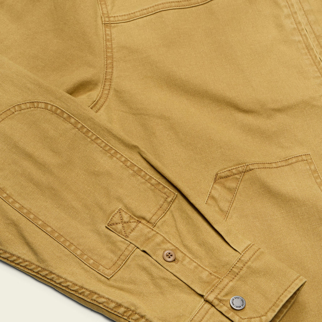 Close-up of a tan canvas garment showing the fabric texture, a buttoned pocket flap, and metal buttons.