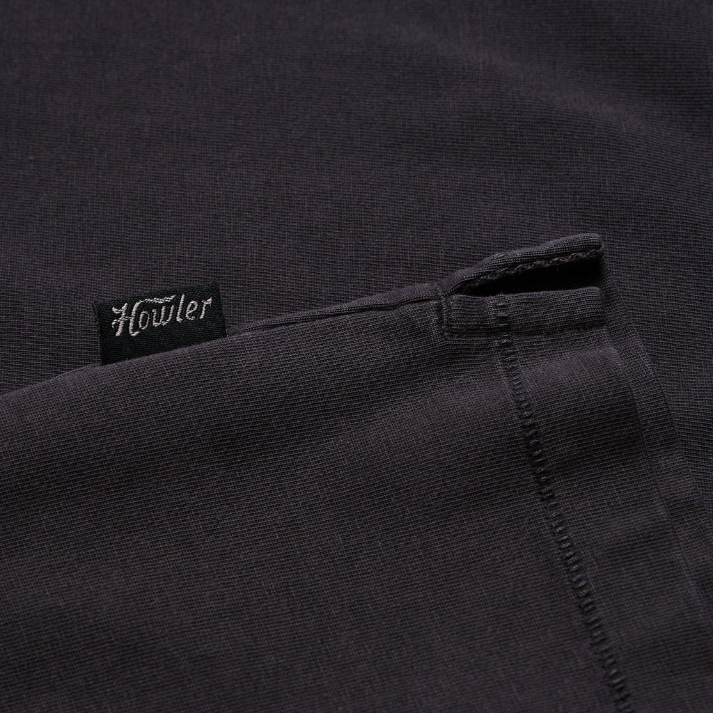 Close-up of a dark charcoal gray knit fabric with a small black fabric tag reading 'Howler' in white script near the upper left area.