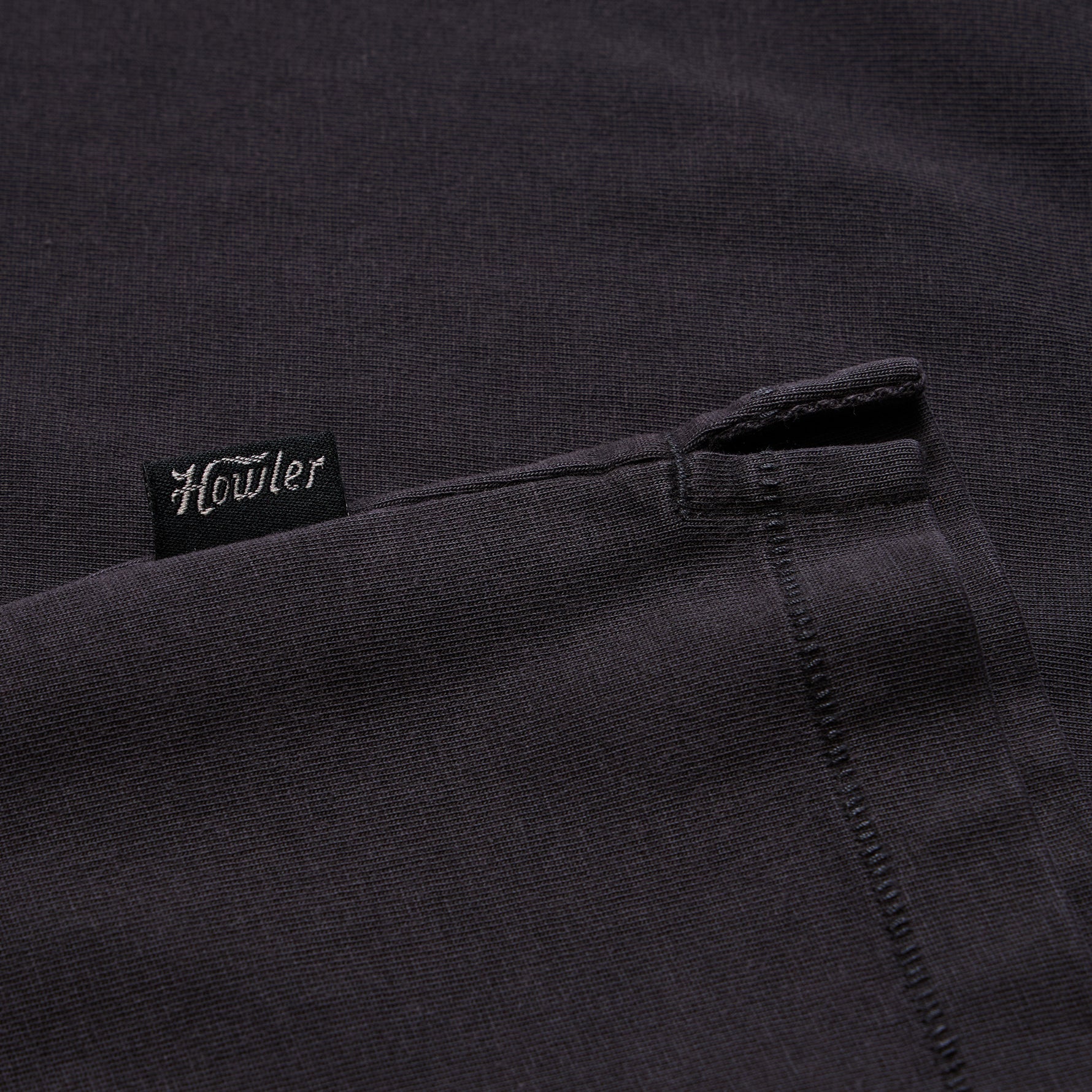 Close-up of a dark charcoal gray knit fabric with a small black fabric tag reading 'Howler' in white script near the upper left area.