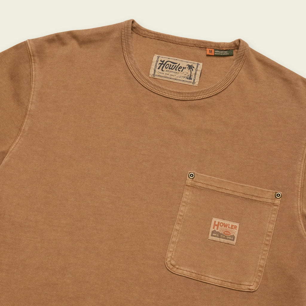 A close-up of a brown cotton crewneck t-shirt with a chest pocket, featuring a visible Howler brand label on the pocket and inner neck tag.