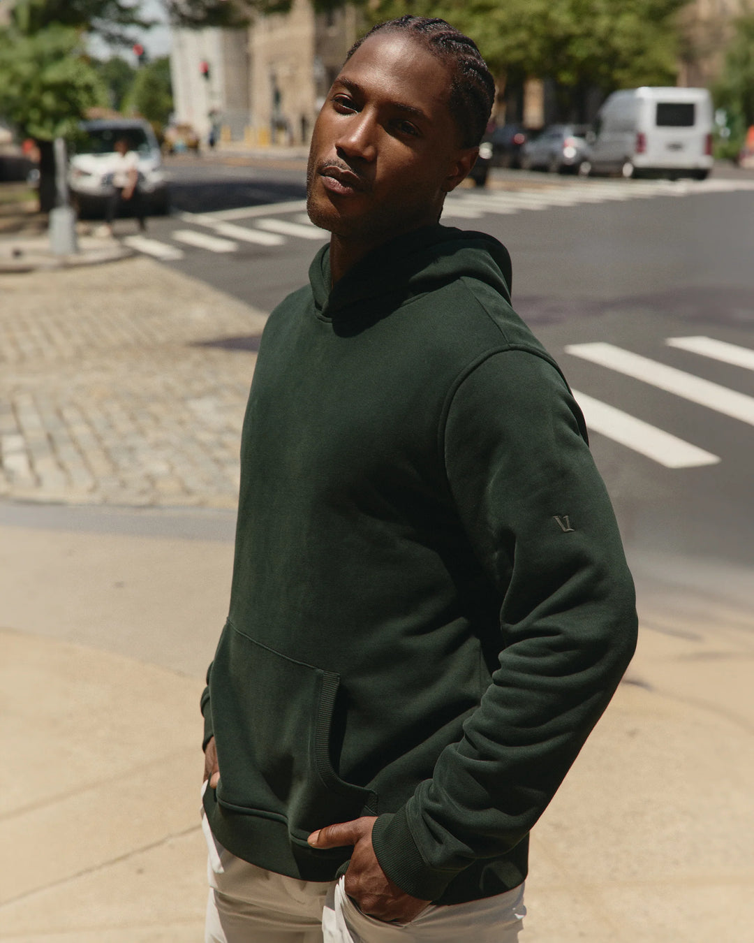 Man wearing a green hoodie standing on a sidewalk with a street in the background