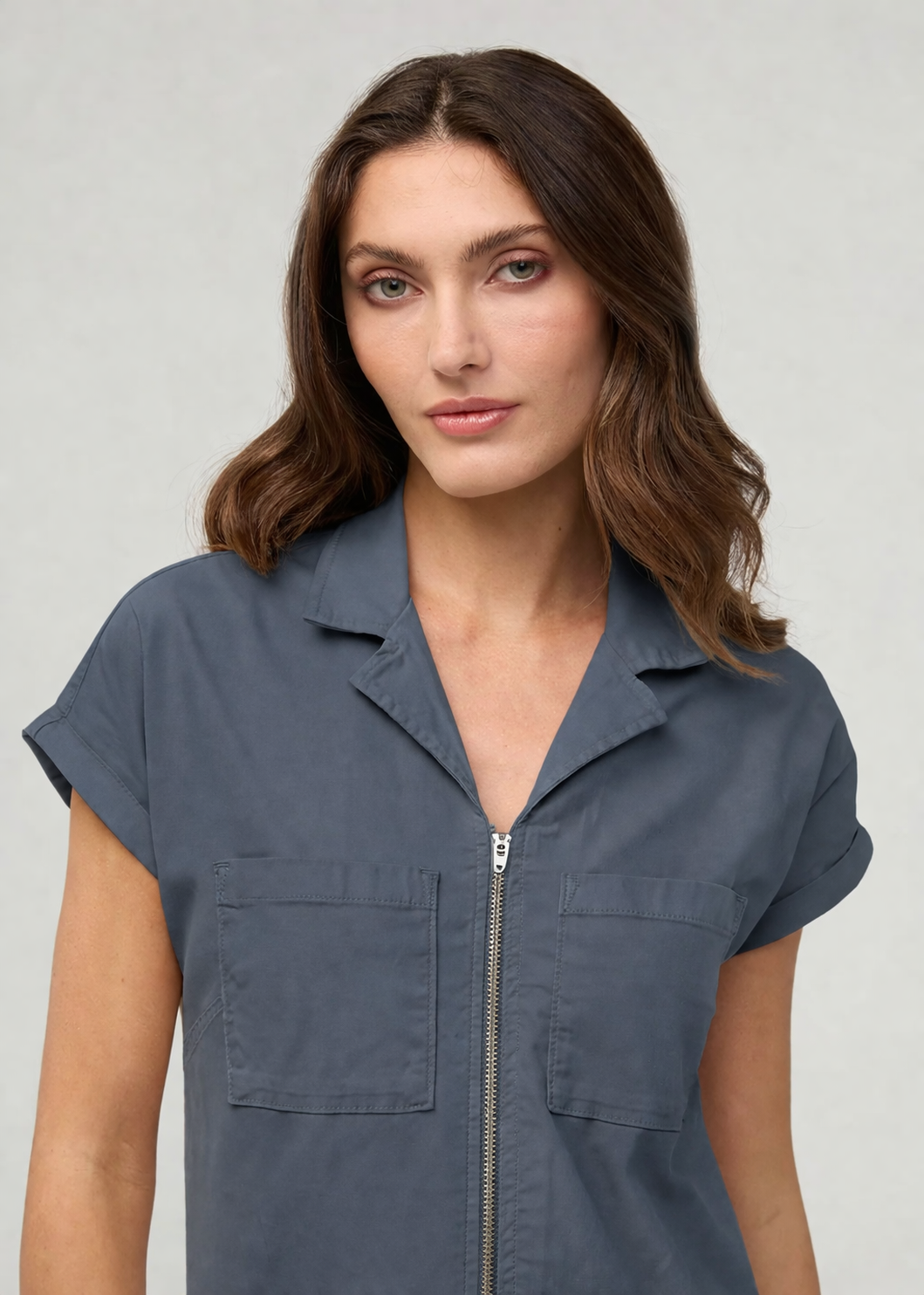 Woman wearing a blue short-sleeve shirt with a zipper on a gray background