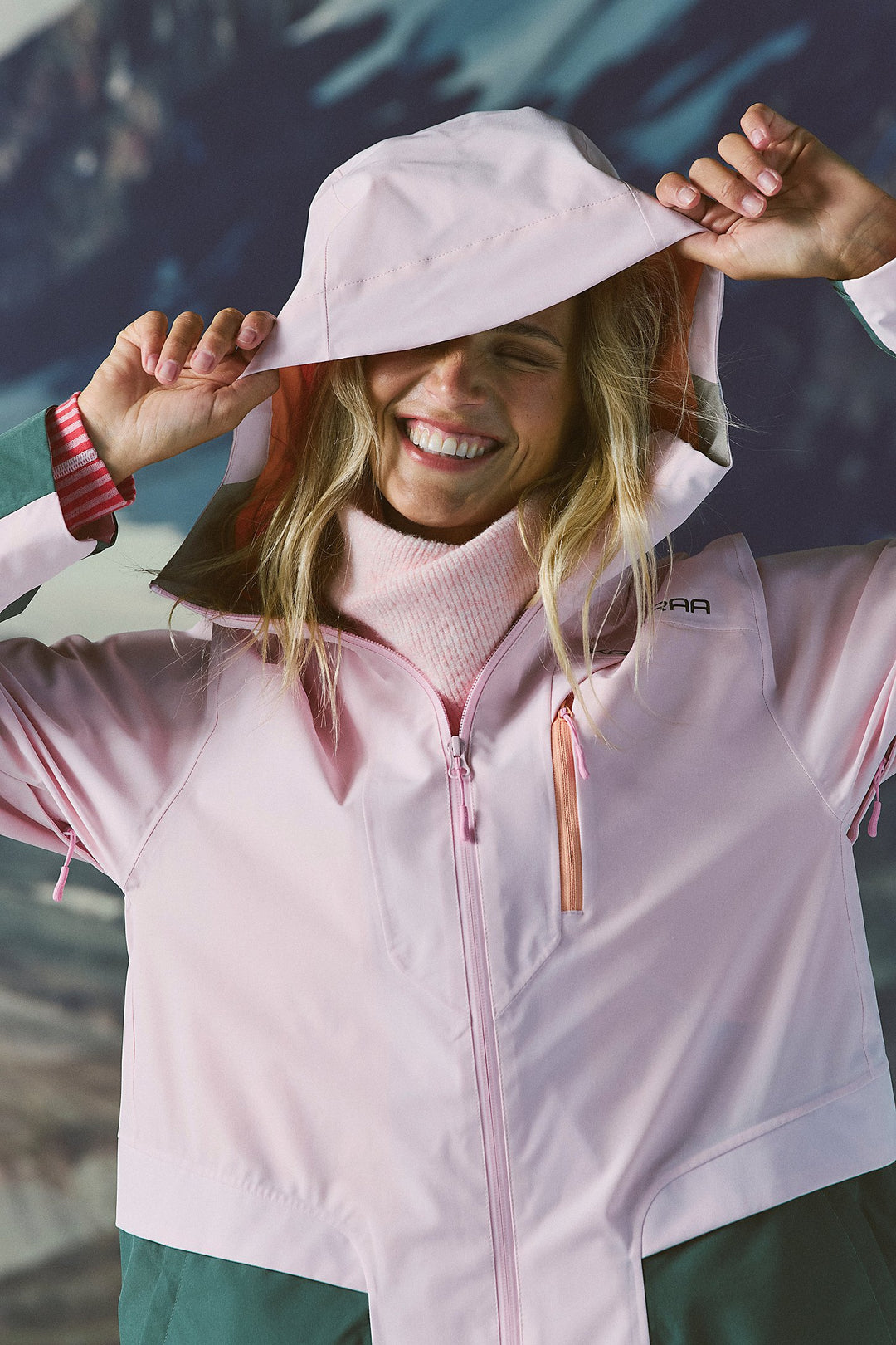 Woman wearing a light pink jacket and hat, standing against a textured wall.