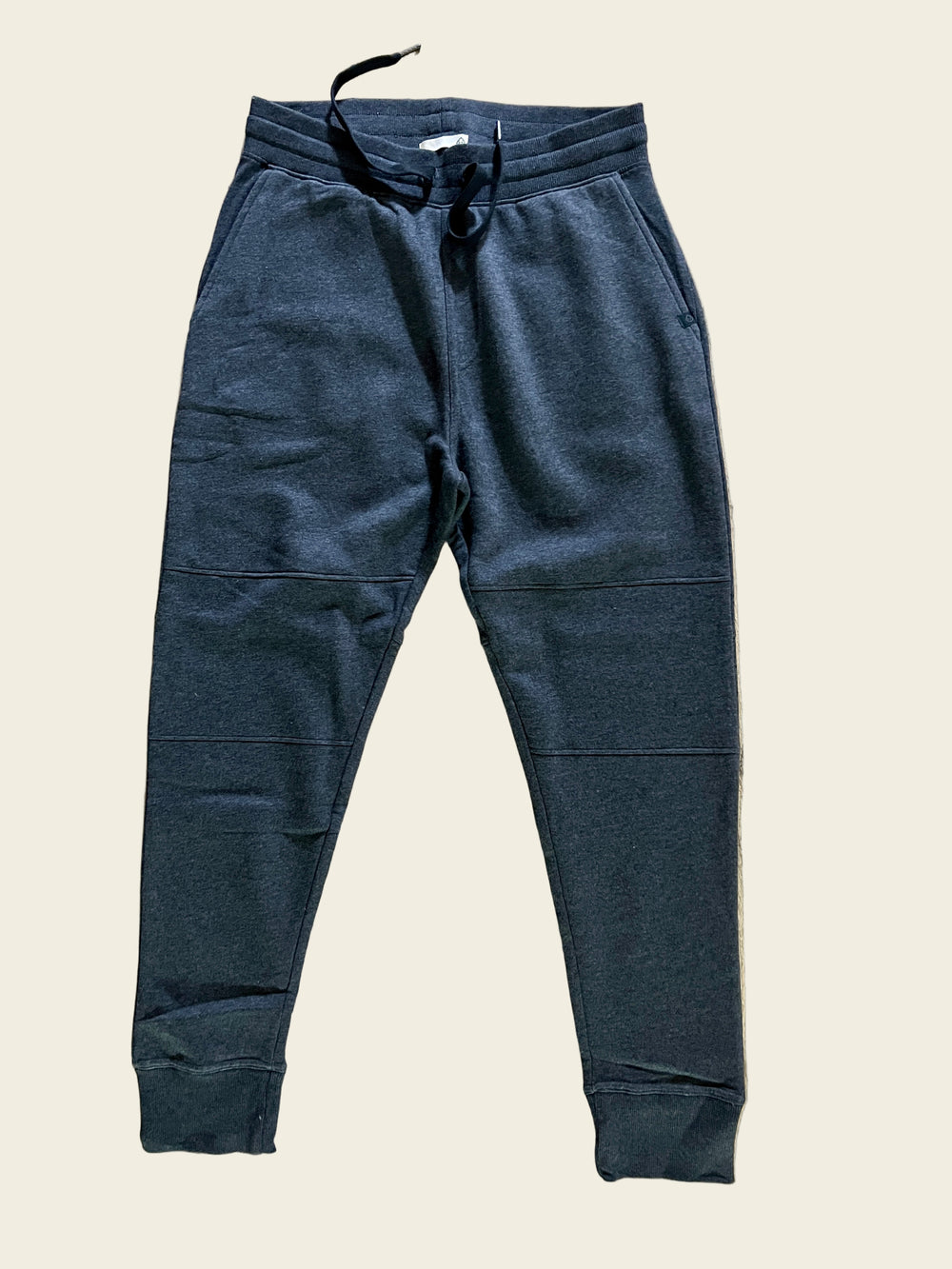 A pair of iron heather Tasc Men's Legendary Fleece Joggers laid flat on a wooden surface.