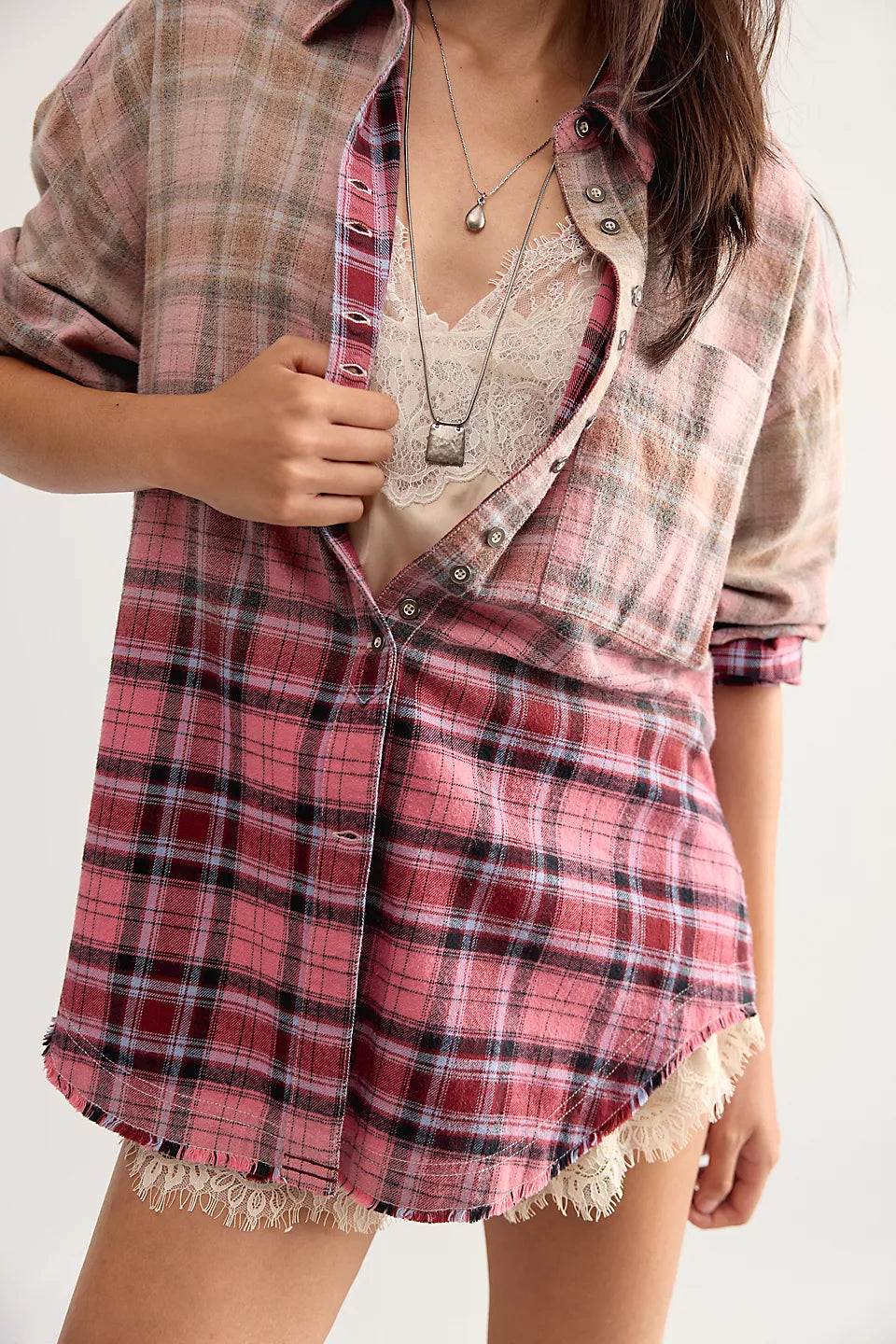 Woman wearing button up pink and beige plaid shirt half opened at front showing lace cream shirt underneath