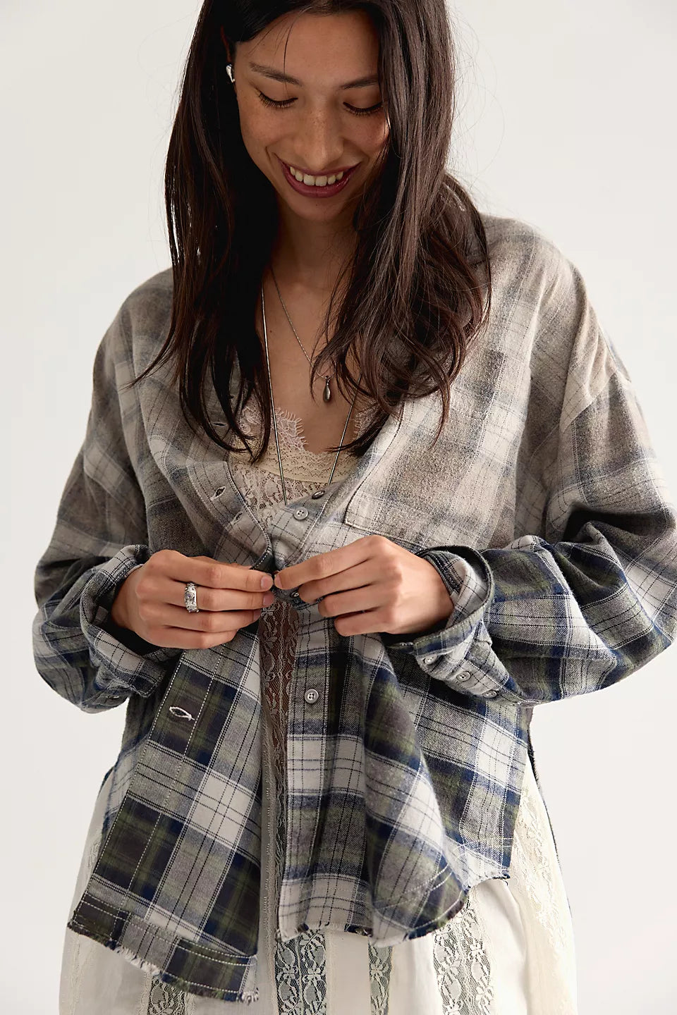 Woman buttoning up a plaid long sleeve shirt with a white lace shirt underneath.