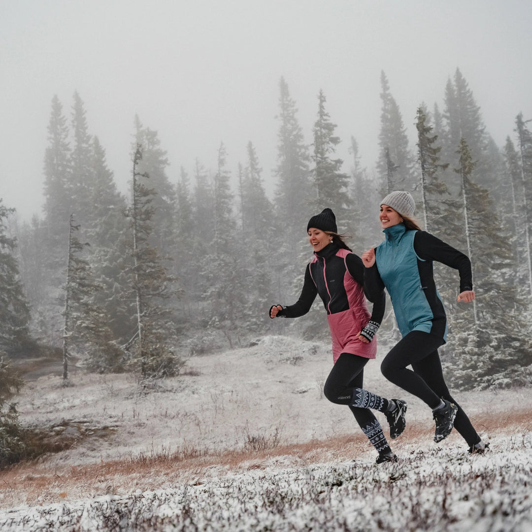 Two people running in a snowy landscape with trees in the background