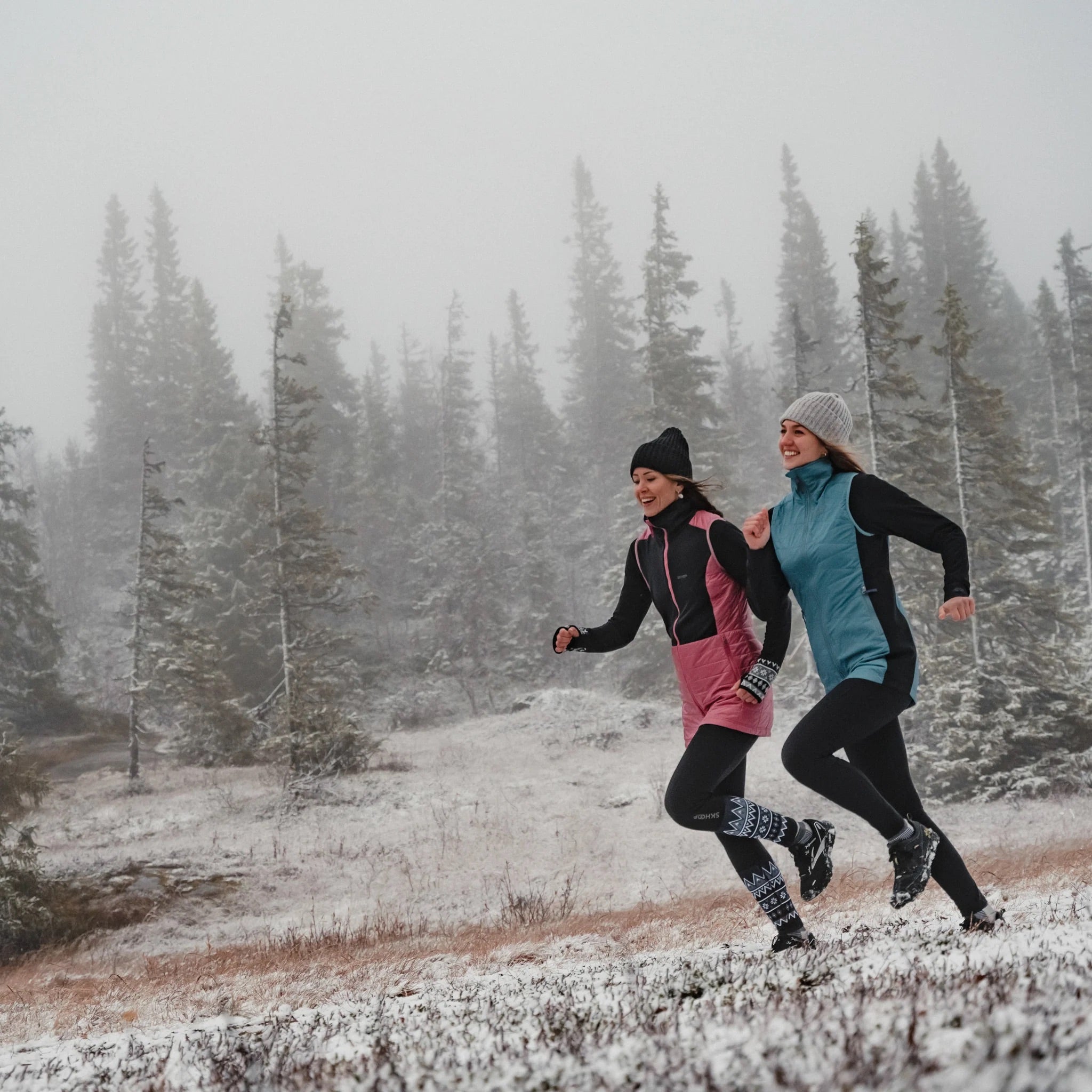 Two people running in a snowy landscape with trees in the background