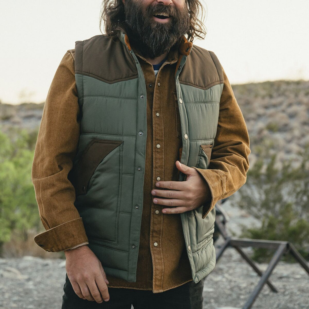 Man wearing a brown jacket and green vest outdoors