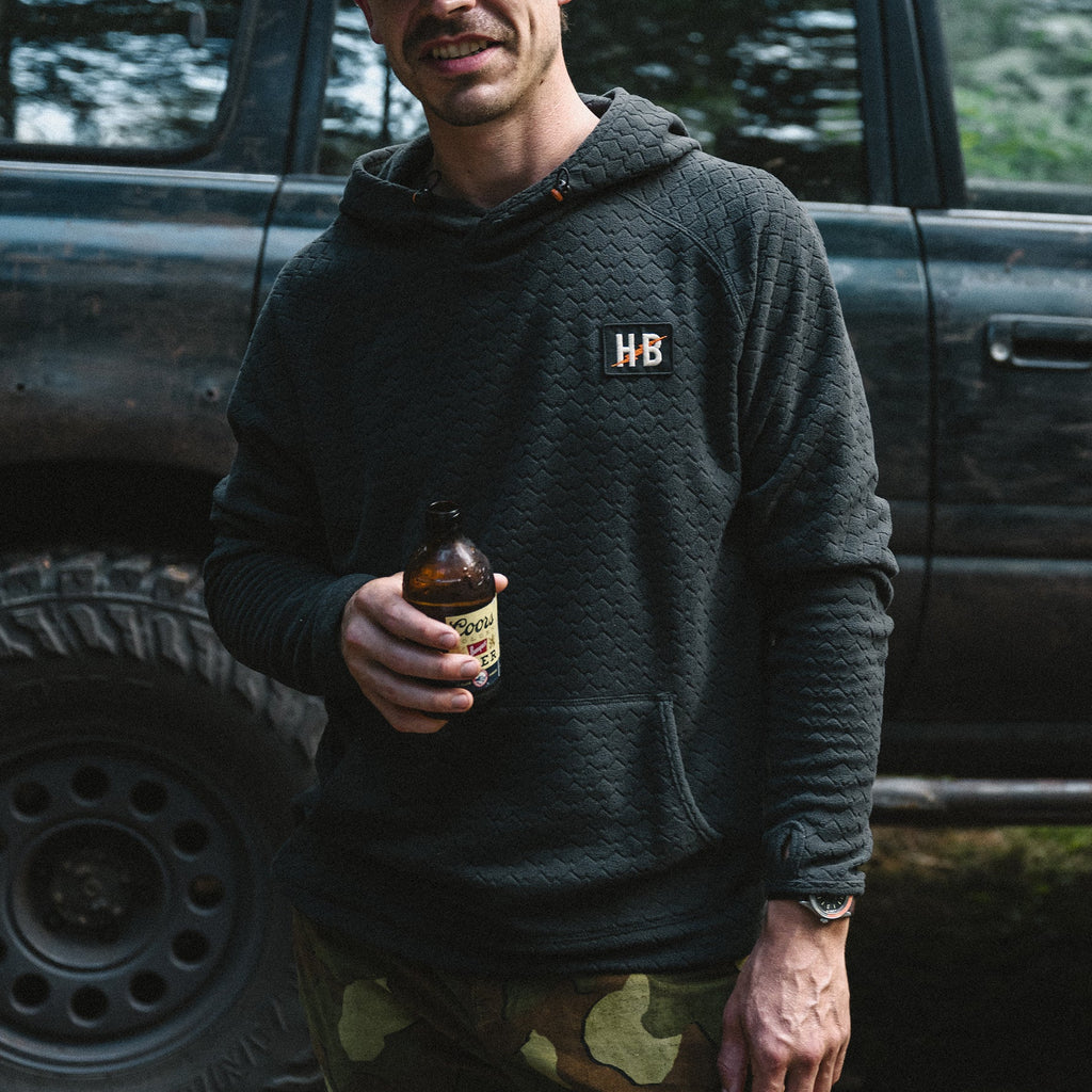 Man holding a bottle in front of a truck with an 'HB' logo on his hoodie.