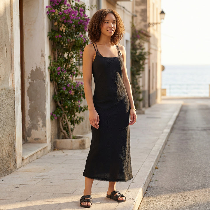 Woman in a black dress standing on a street with buildings and flowers in the background