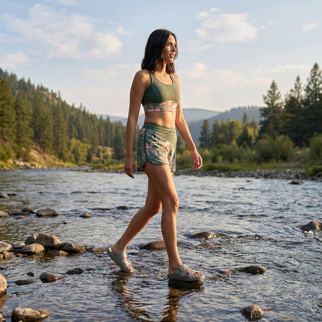Woman walking through a river with a forest and mountains in the background