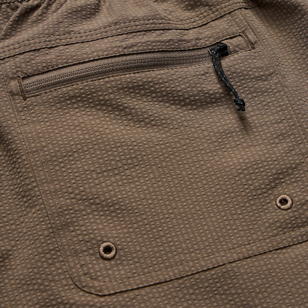 Close-up of a brown textured fabric pocket with a zipper and button details.
