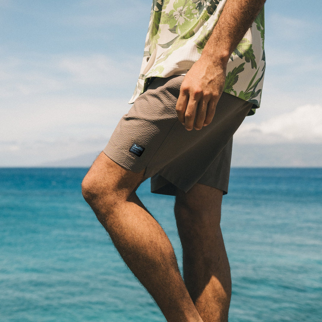 Person wearing a floral shirt and beige shorts with a blue ocean and sky background