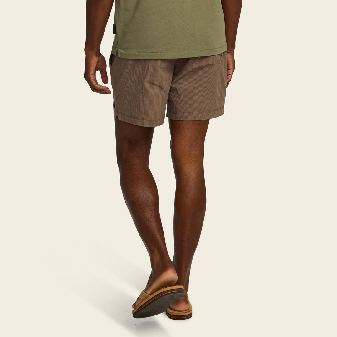 Person wearing brown shorts and green shirt on a beige background