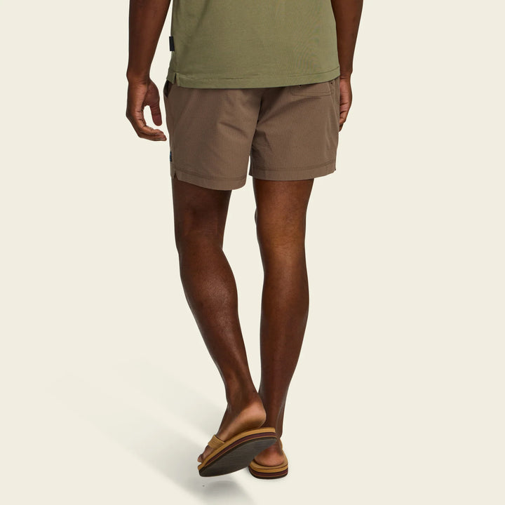 Person wearing brown shorts and green shirt on a beige background