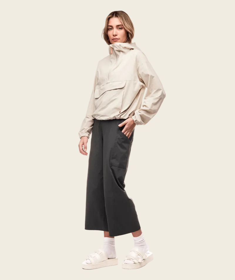 Person wearing a beige jacket and black pants on a white background