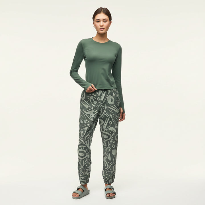 Woman wearing a green long-sleeve top and patterned pants on a white background