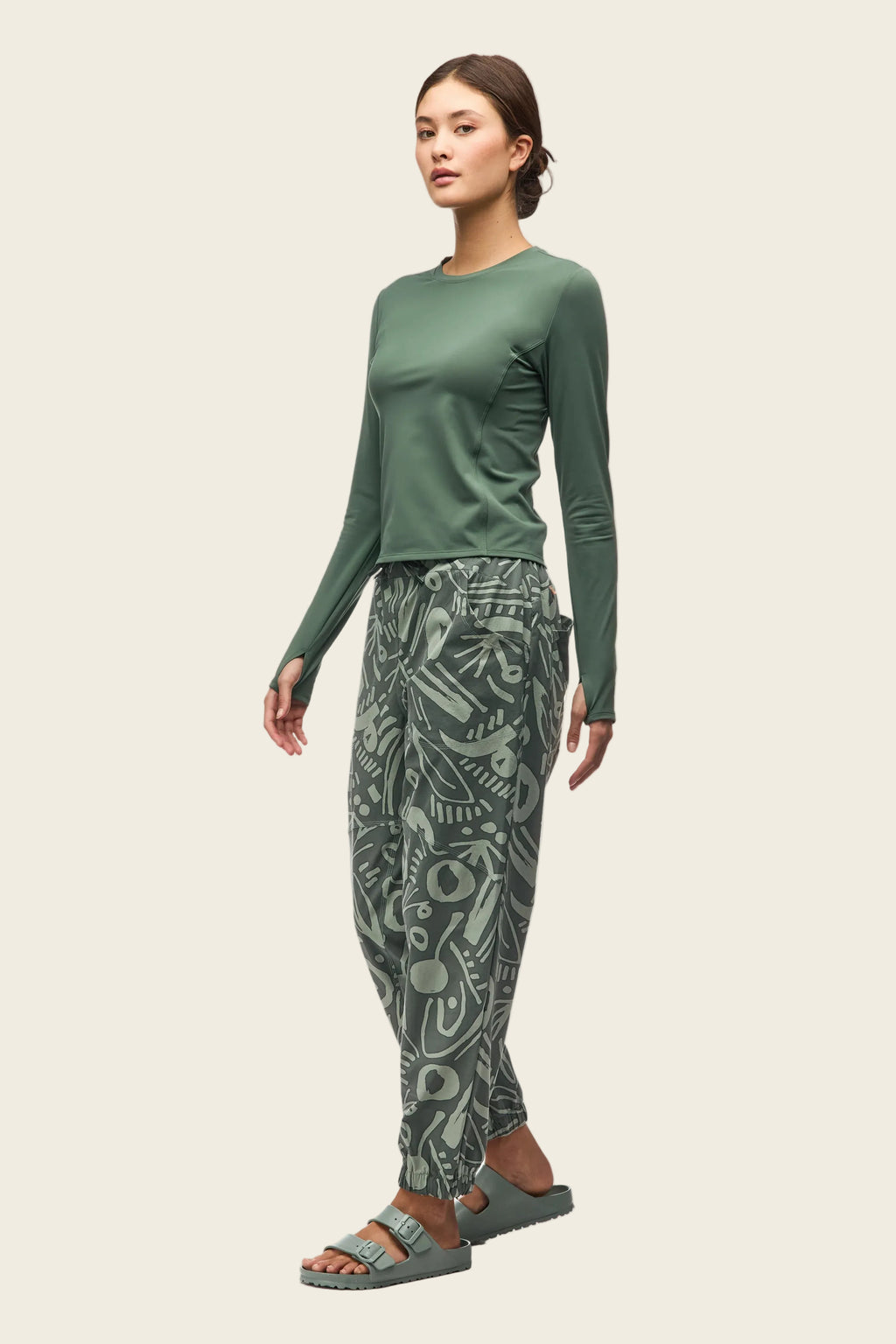 Woman wearing a green long-sleeve top and patterned pants on a white background