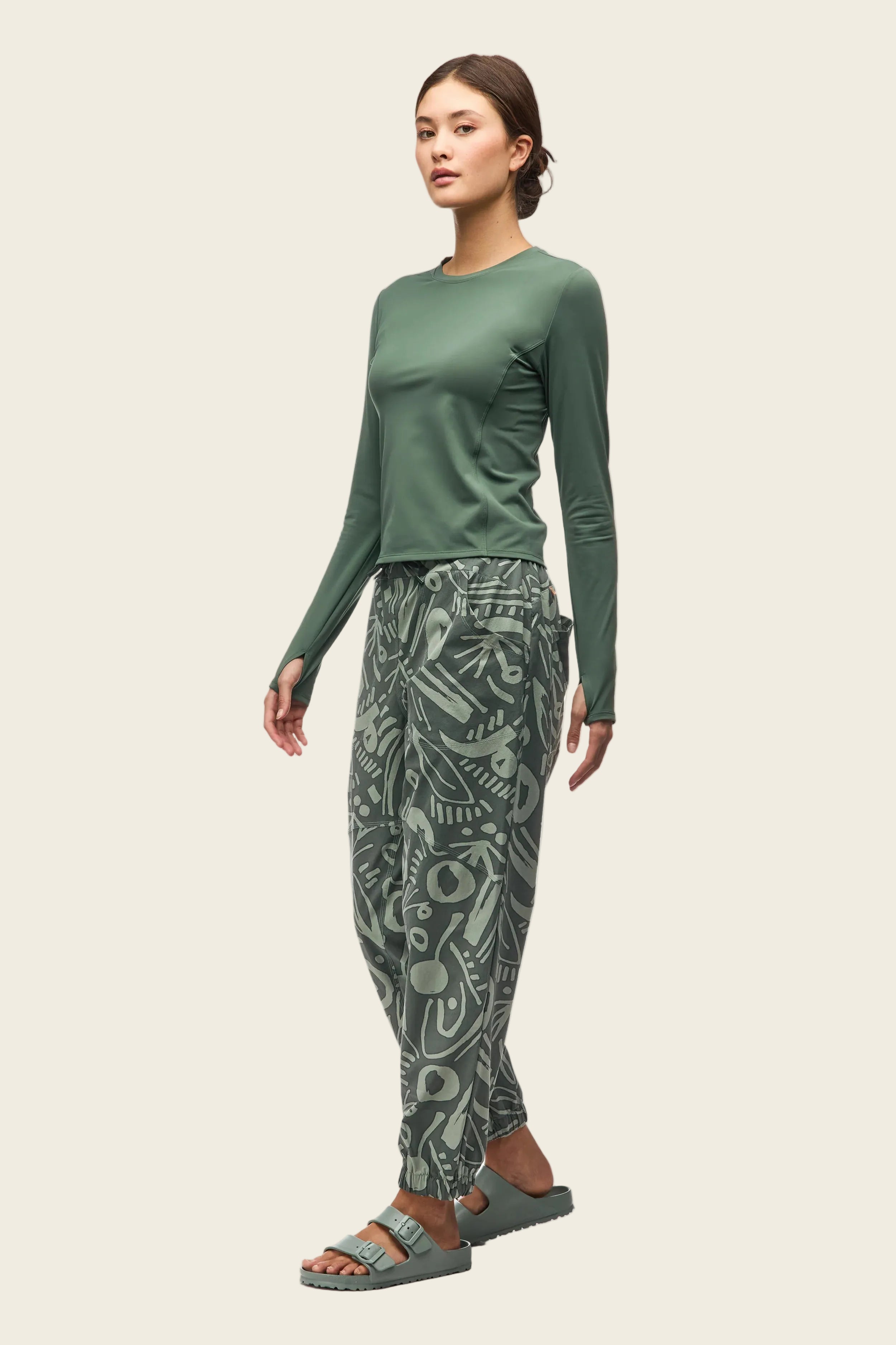 Woman wearing a green long-sleeve top and patterned pants on a white background