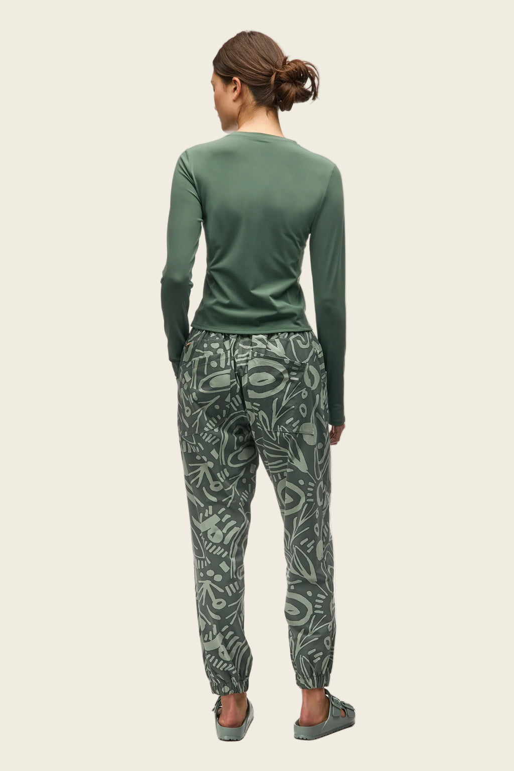 Person wearing a green long-sleeve top and patterned pants on a white background