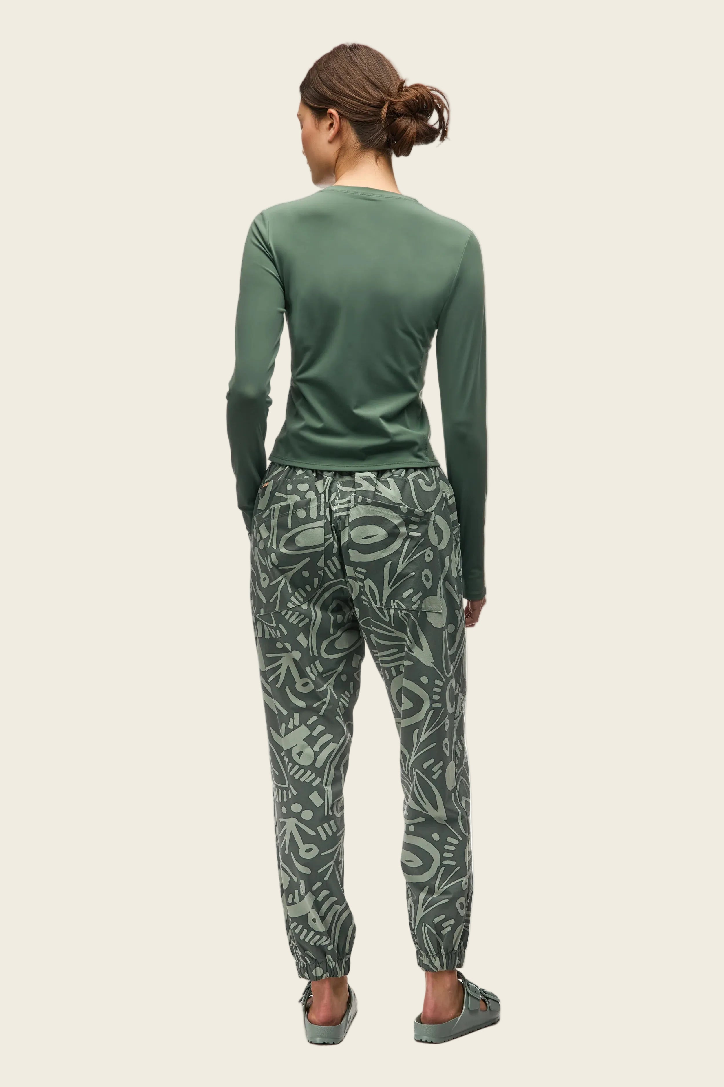 Person wearing a green long-sleeve top and patterned pants on a white background