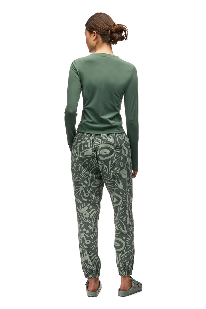 Person wearing a green long-sleeve top and patterned pants on a white background