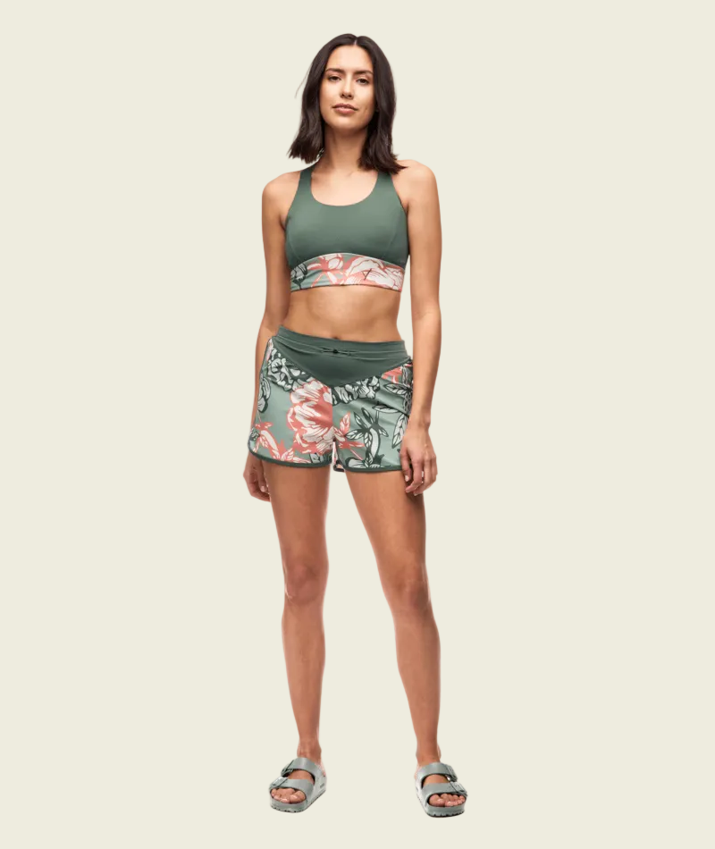 Woman wearing a green sports bra and floral shorts on a white background
