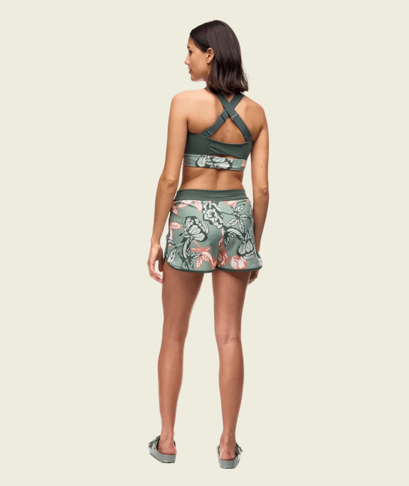 Woman wearing a green sports bra and shorts with floral pattern on a white background