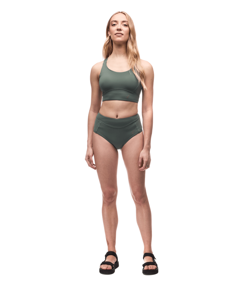 Woman wearing a green sports bra and high-waisted shorts on a white background