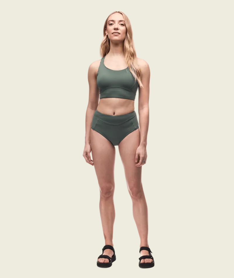 Woman wearing a green sports bra and high-waisted shorts on a white background