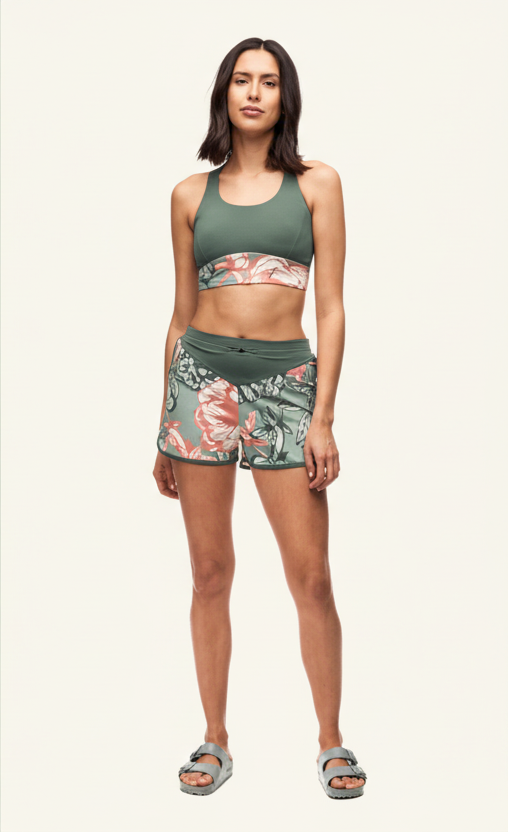 Woman wearing a green sports bra and floral shorts on a white background