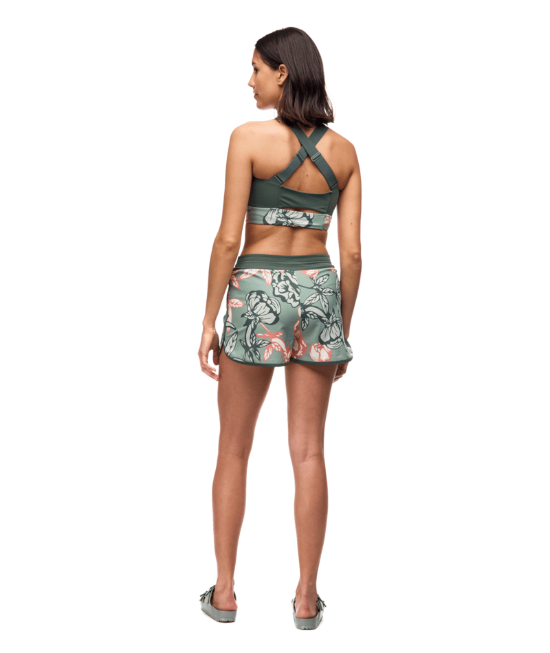 Woman wearing a green sports bra and shorts with floral pattern on a white background